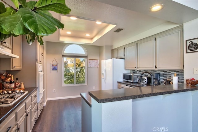 kitchen featuring dark countertops, visible vents, a tray ceiling, appliances with stainless steel finishes, and a peninsula