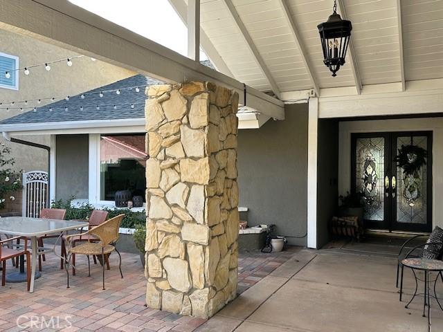 doorway to property with outdoor dining area, french doors, roof with shingles, stucco siding, and a patio area