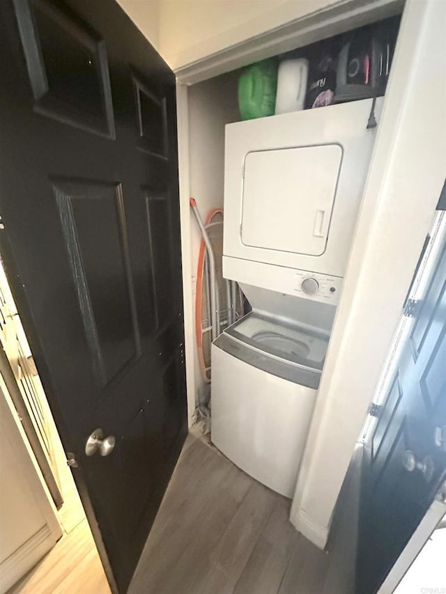 clothes washing area featuring laundry area, stacked washing maching and dryer, and wood finished floors