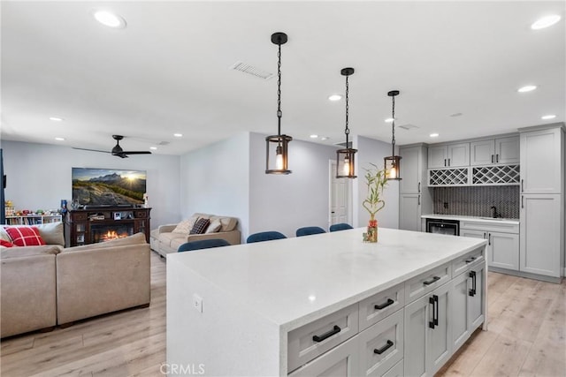 kitchen featuring a glass covered fireplace, decorative backsplash, light wood-style flooring, and a center island