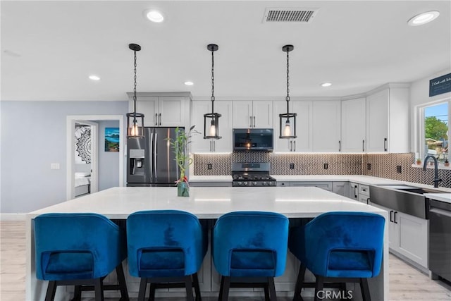 kitchen with visible vents, a kitchen island, a sink, appliances with stainless steel finishes, and backsplash