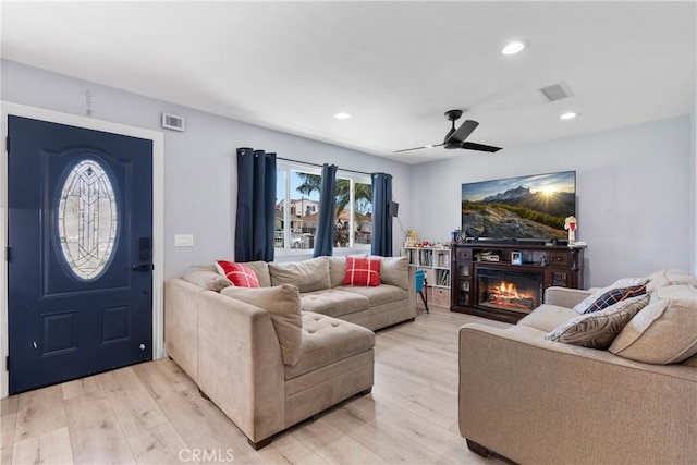 living area featuring visible vents, recessed lighting, light wood-type flooring, and a glass covered fireplace