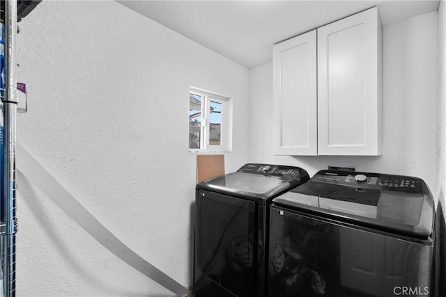 washroom featuring washer and dryer, cabinet space, and a textured wall