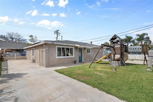 exterior space featuring stucco siding, a playground, a front yard, and fence