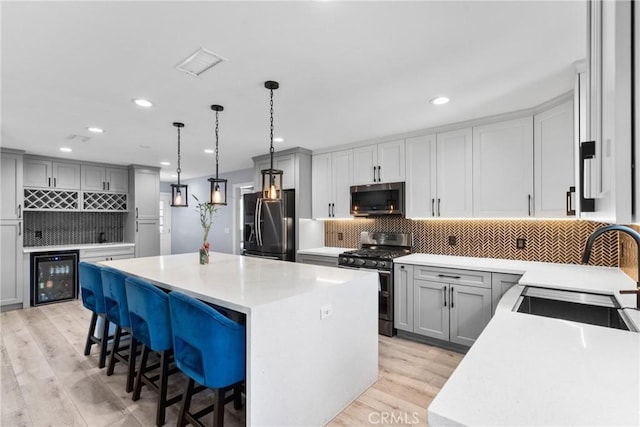 kitchen featuring a sink, stainless steel appliances, wine cooler, a kitchen breakfast bar, and a center island