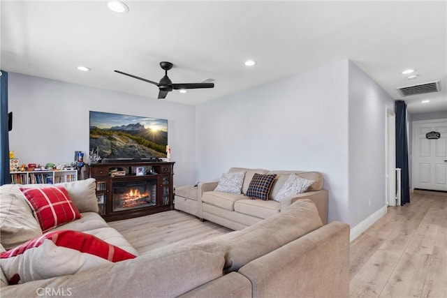 living room featuring visible vents, a glass covered fireplace, recessed lighting, light wood finished floors, and baseboards