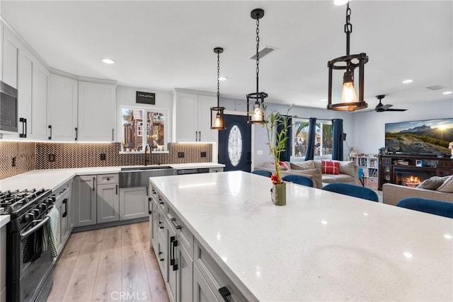 kitchen featuring light wood finished floors, a warm lit fireplace, a sink, black gas range, and open floor plan