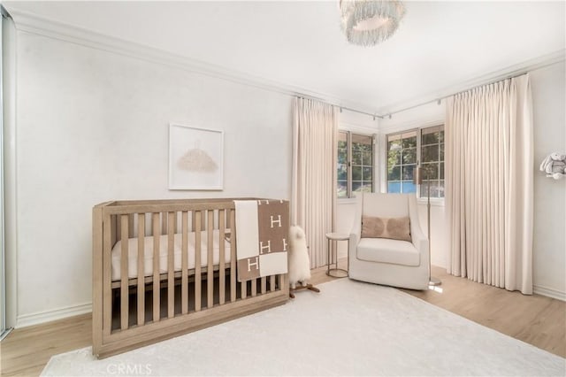 bedroom featuring crown molding, a crib, baseboards, and wood finished floors