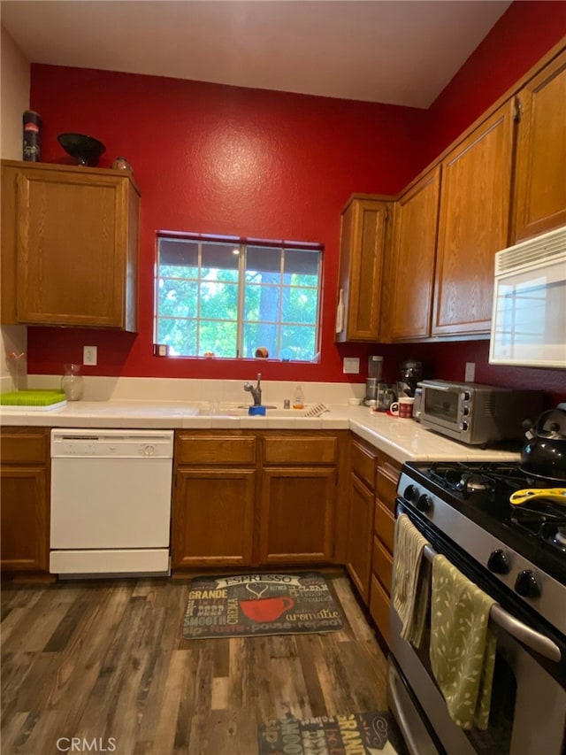 kitchen with white appliances, dark wood-type flooring, a sink, and light countertops