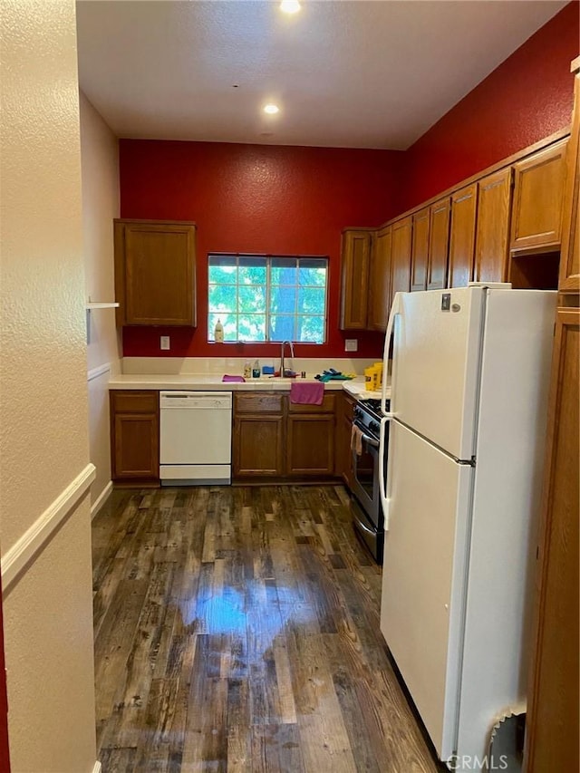 kitchen featuring dark wood-style floors, white appliances, brown cabinetry, and a sink