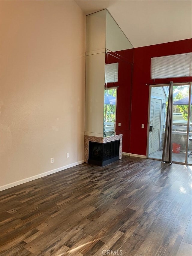 unfurnished living room with dark wood-style flooring, a wealth of natural light, and baseboards