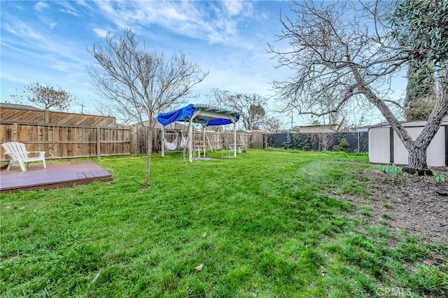 view of yard with a fenced backyard, an outdoor structure, a deck, and a storage shed