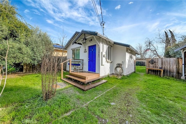 rear view of property featuring stucco siding, a yard, and fence