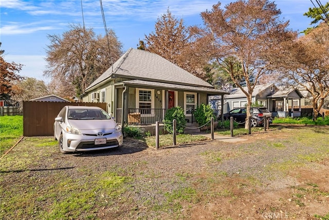 view of side of home with covered porch, a shingled roof, and fence