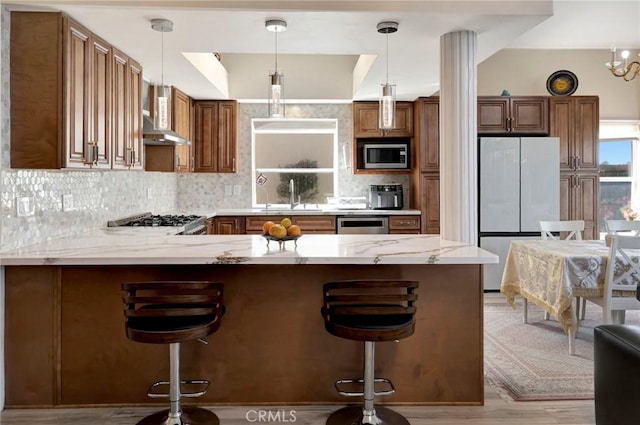 kitchen featuring a peninsula, a sink, freestanding refrigerator, tasteful backsplash, and stainless steel microwave