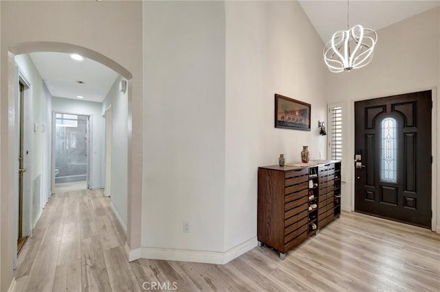 entrance foyer with arched walkways, a chandelier, baseboards, light wood-style flooring, and high vaulted ceiling