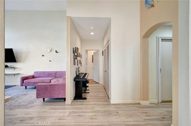 hallway with light wood-type flooring, baseboards, and arched walkways