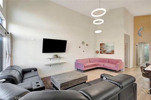 living area with high vaulted ceiling, arched walkways, baseboards, and light wood finished floors