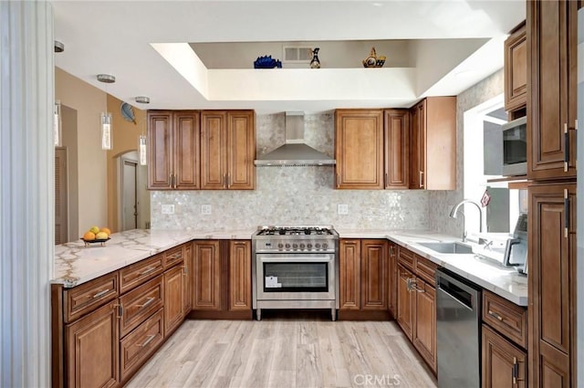 kitchen with wall chimney range hood, stainless steel appliances, a sink, and brown cabinetry