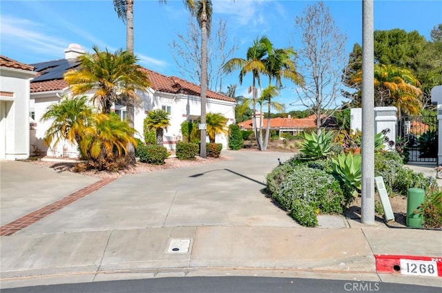 view of front of home with stucco siding, fence, a tile roof, and roof mounted solar panels