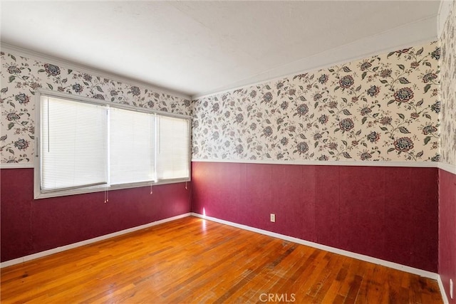 spare room featuring wallpapered walls, wood-type flooring, baseboards, and wainscoting