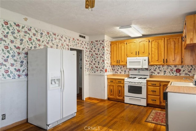 kitchen featuring a sink, white appliances, wallpapered walls, and wainscoting