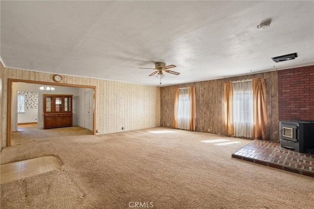 unfurnished living room featuring ceiling fan, carpet, a wood stove, and wooden walls