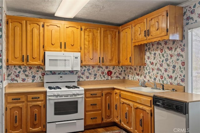 kitchen with white appliances, a sink, light countertops, brown cabinetry, and wallpapered walls