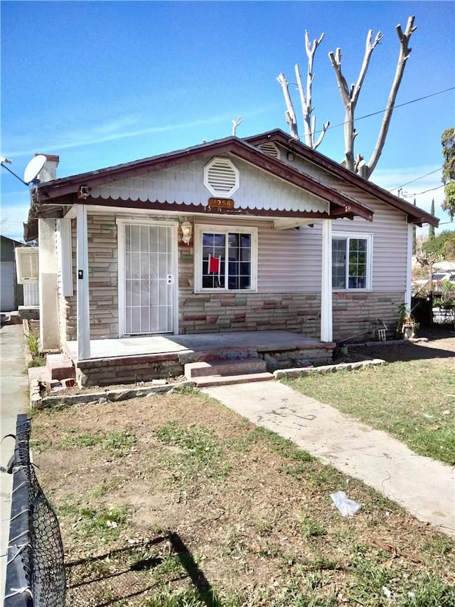 bungalow-style house with stone siding, a porch, and a front yard