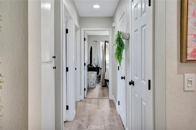 hallway with light wood-style flooring and a textured wall