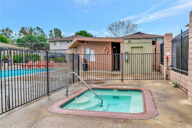 community pool with a patio area, fence, and a hot tub