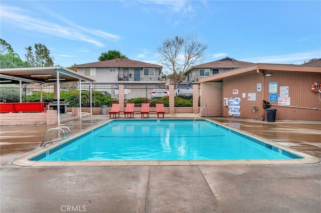 pool with a patio, fence, and a grill