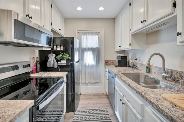 kitchen featuring recessed lighting, stainless steel appliances, a sink, white cabinetry, and light wood-style floors