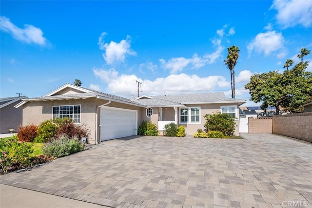 ranch-style house featuring a garage, decorative driveway, fence, and stucco siding