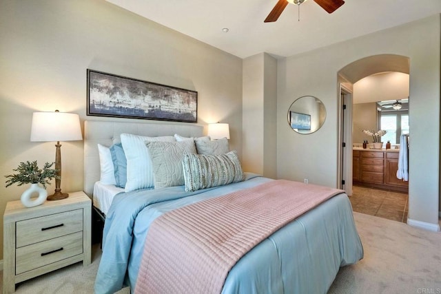 bedroom with light carpet, arched walkways, ceiling fan, ensuite bathroom, and light tile patterned flooring