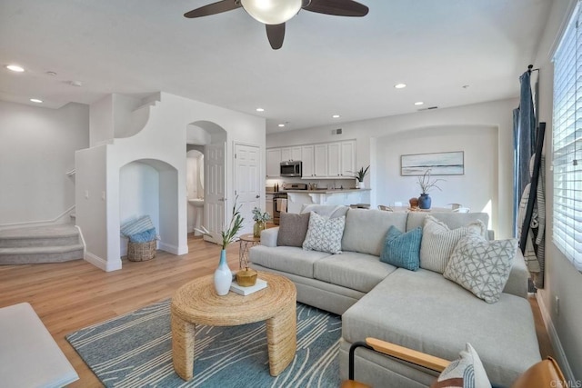 living area featuring arched walkways, recessed lighting, baseboards, stairs, and light wood-style floors