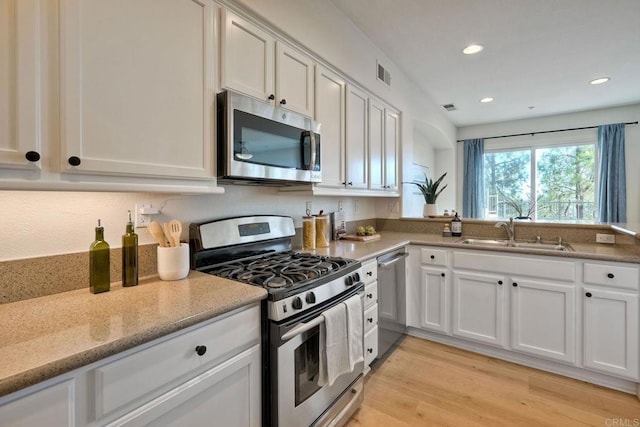 kitchen featuring light wood finished floors, visible vents, appliances with stainless steel finishes, white cabinets, and a sink