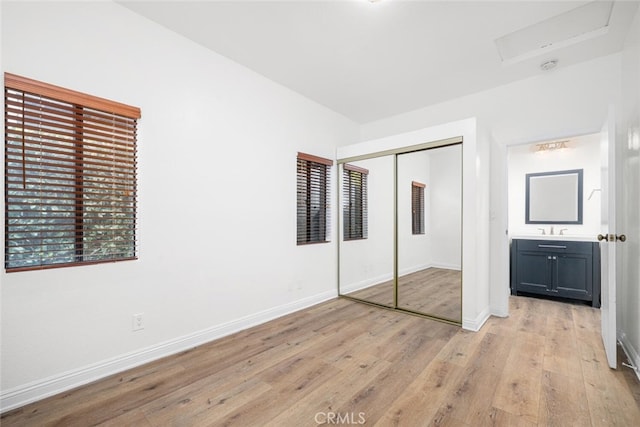 unfurnished bedroom with light wood-type flooring, a sink, baseboards, and a closet