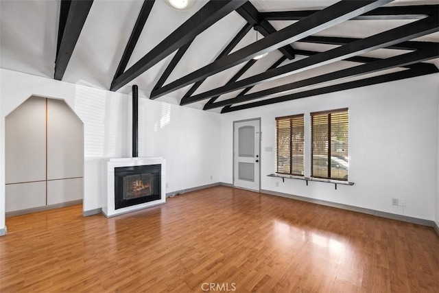 unfurnished living room featuring lofted ceiling with beams, wood finished floors, and baseboards