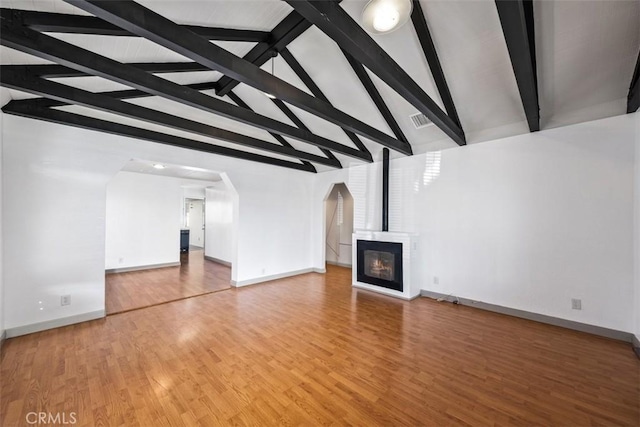 unfurnished living room with lofted ceiling with beams, light wood-style flooring, arched walkways, and baseboards