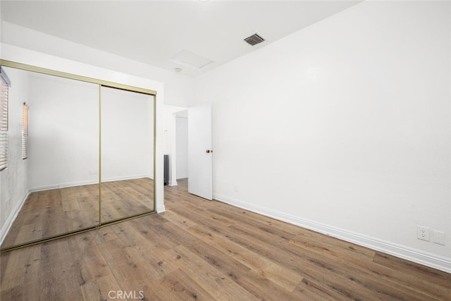 unfurnished bedroom featuring attic access, baseboards, visible vents, wood finished floors, and a closet