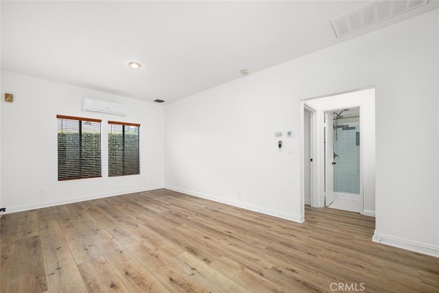 unfurnished room with wood finished floors, visible vents, baseboards, and a wall mounted AC