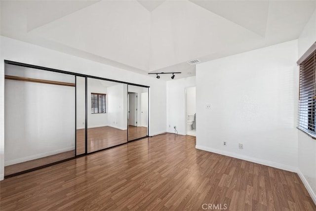 unfurnished bedroom with wood finished floors, visible vents, baseboards, multiple windows, and rail lighting