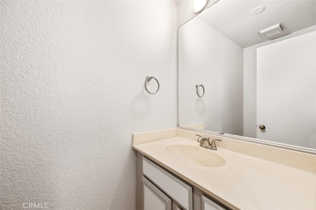 bathroom with visible vents, a textured wall, and vanity