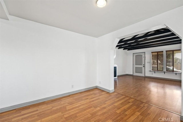 spare room with light wood-type flooring, baseboards, and beamed ceiling