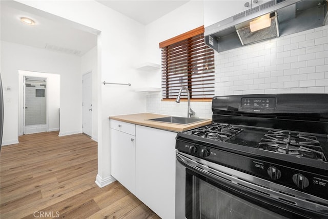 kitchen with stainless steel gas range oven, under cabinet range hood, a sink, white cabinetry, and light wood-type flooring