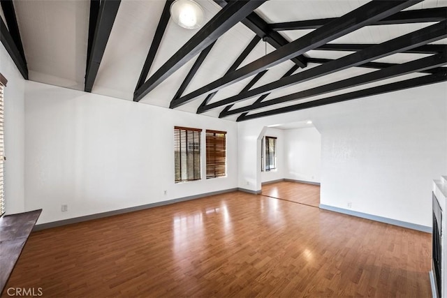 unfurnished living room featuring lofted ceiling with beams, light wood finished floors, and baseboards