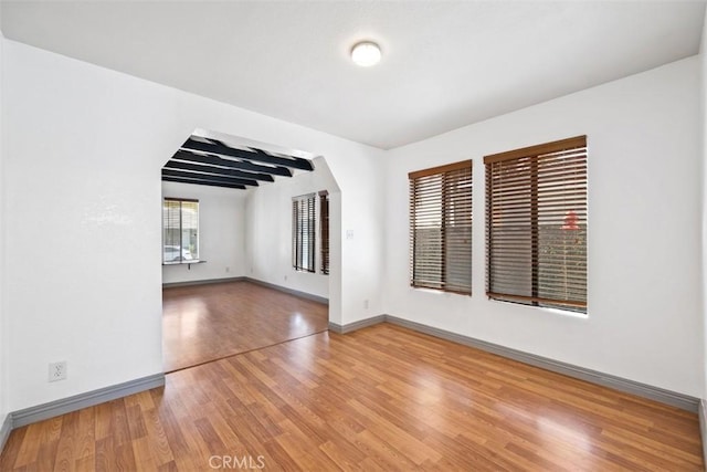 empty room featuring arched walkways, wood finished floors, and baseboards