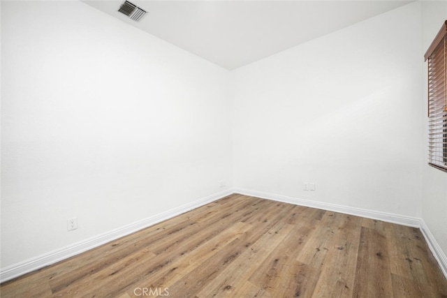 spare room with light wood-type flooring, visible vents, and baseboards