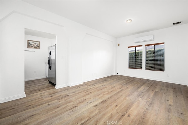 spare room featuring a wall unit AC, visible vents, baseboards, and wood finished floors